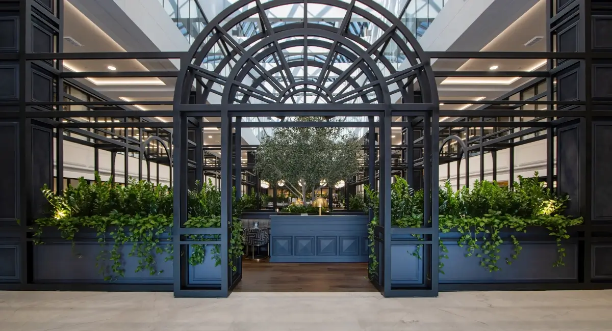 Grand architectural entrance to an atrium lounge with dark metal framing and built-in planters.
