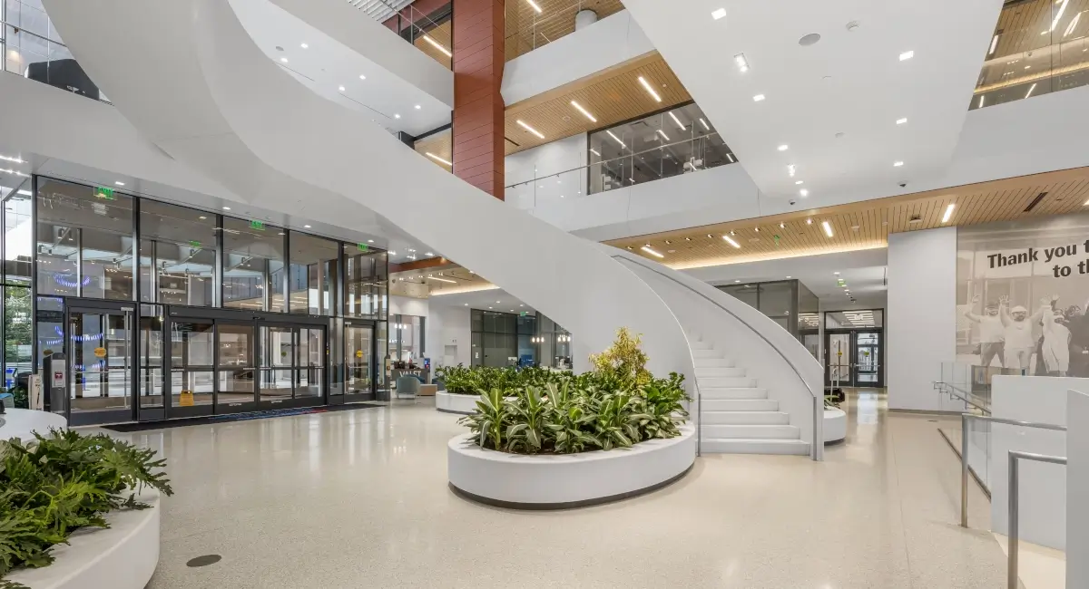 Wide view of a contemporary hospital lobby showing integrated plant beds at the base of a grand white staircase.