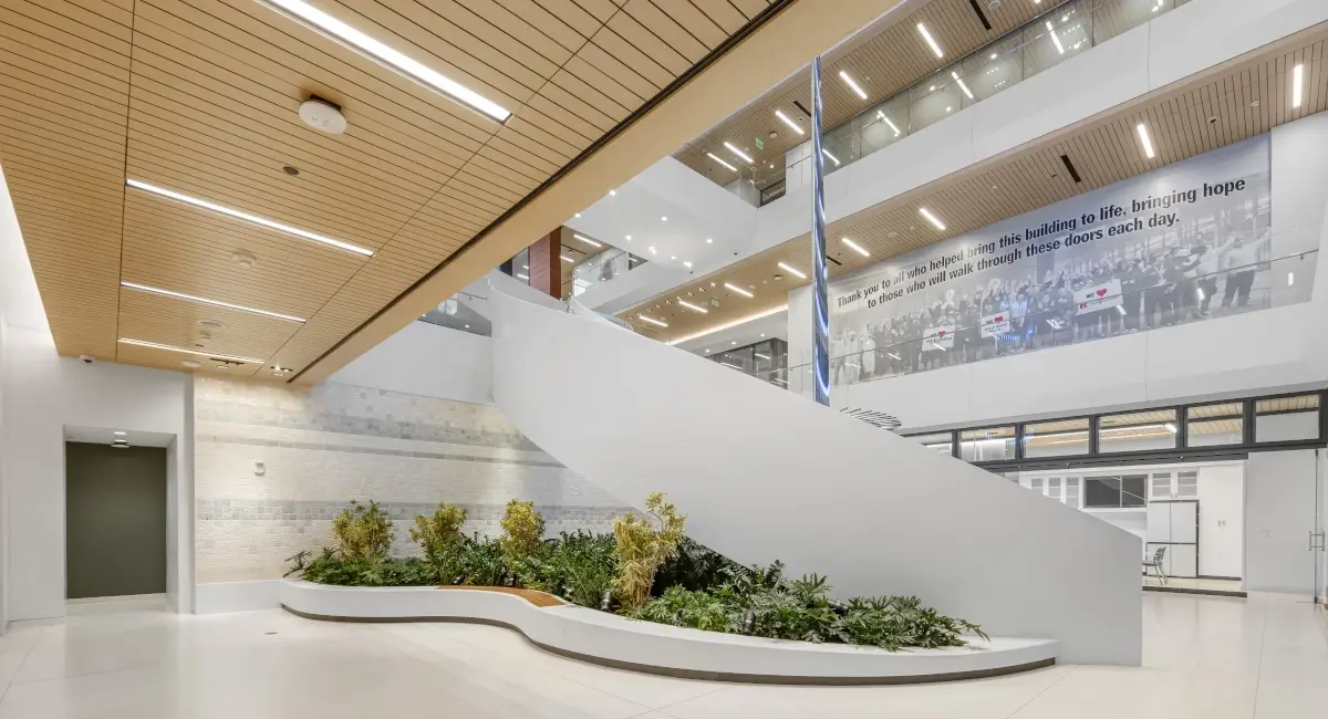 Bright, multi-story atrium with a white winding staircase and a curved architectural planter with indoor greenery.