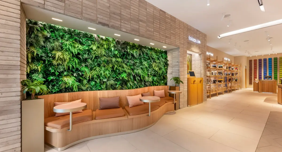 Modern Nespresso boutique lounge area featuring a curved wooden bench and a large lush living wall of ferns.