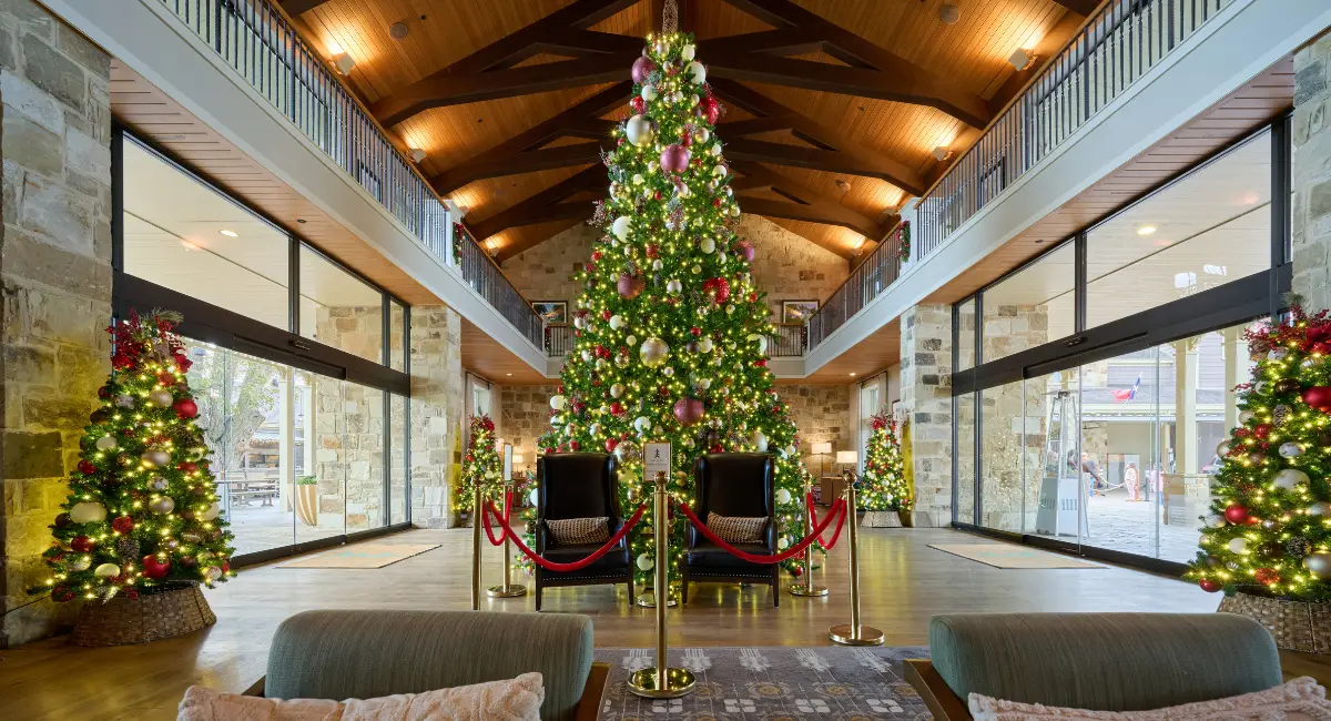Multiple festive holiday decorations in a large hotel lobby surrounding a large 20-foot tall centerpiece Christmas tree.