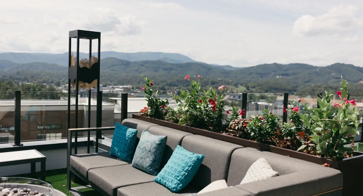 Rooftop patio seating with colorful pillows and flowering planters against a scenic mountain backdrop.