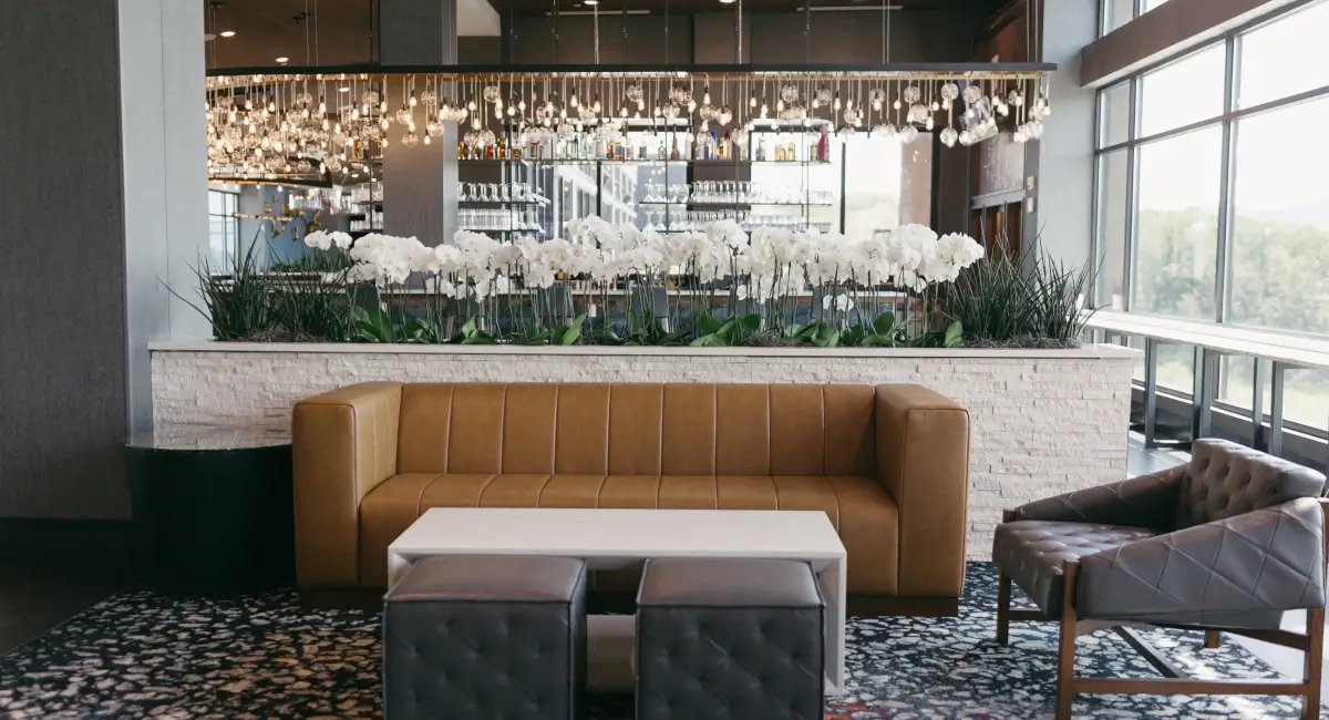 Modern hotel bar and lounge area featuring a long planter of white orchids behind a tan leather sofa.