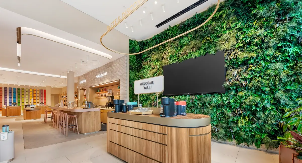 Nespresso tasting bar with wooden cabinetry set against a vibrant floor-to-ceiling indoor vertical garden.