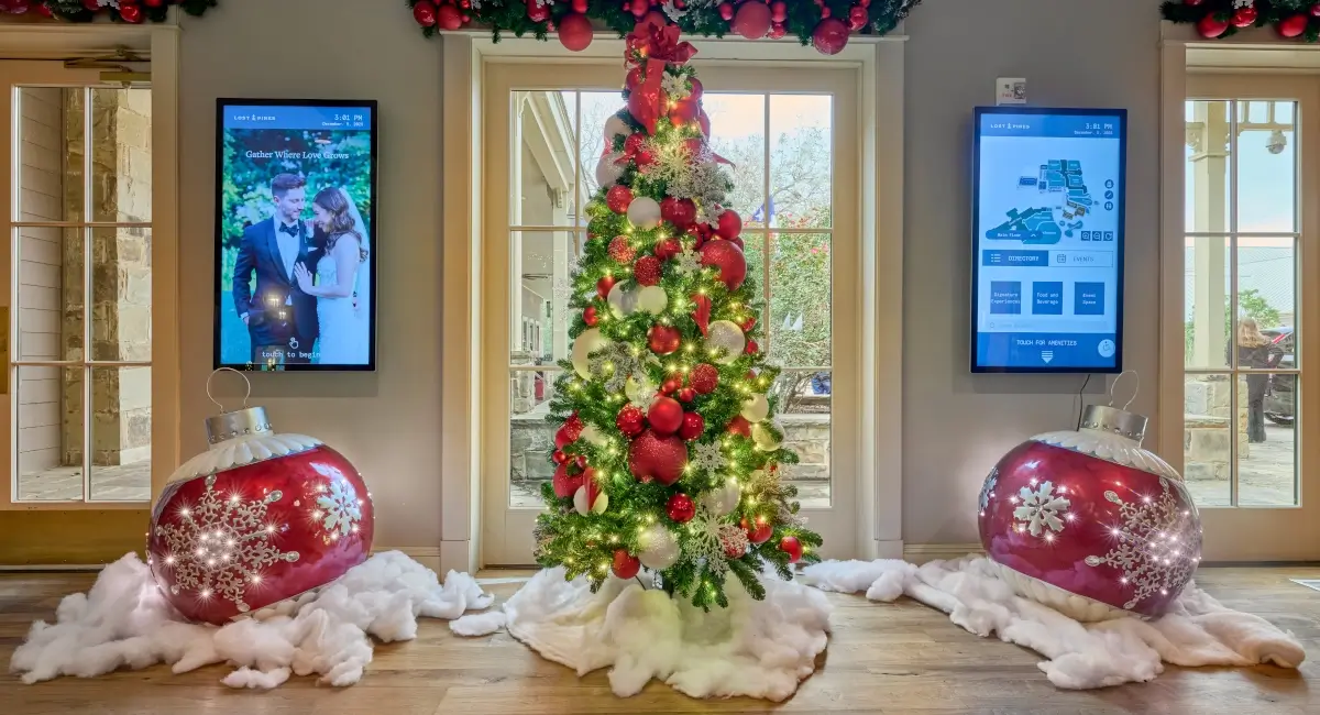 A decorated Christmas tree flanked by two large light-up red ornaments and digital display screens.