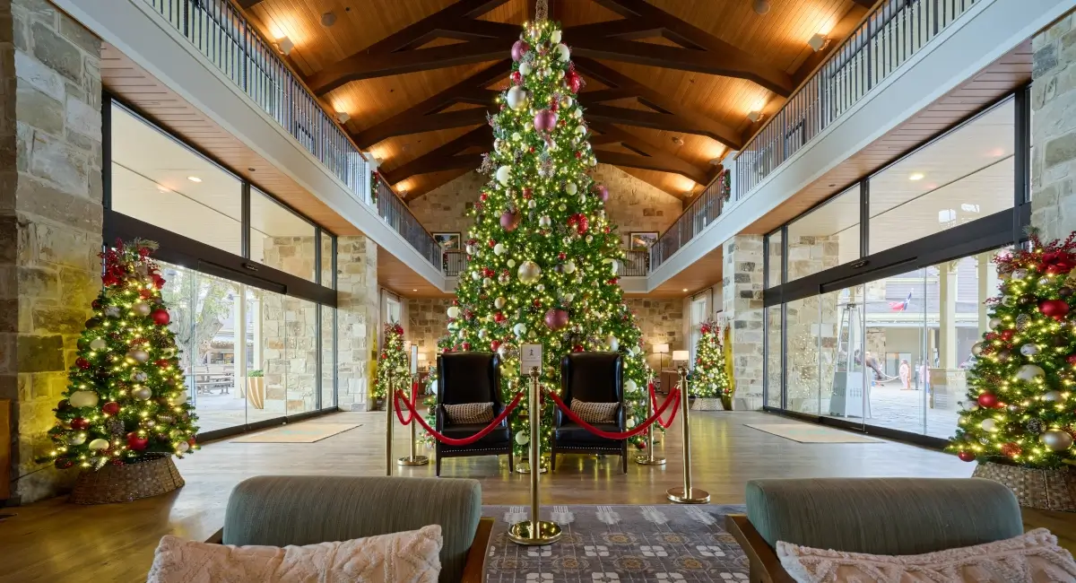 A massive, brightly lit Christmas tree in a luxury lodge lobby with vaulted ceilings and stone walls.