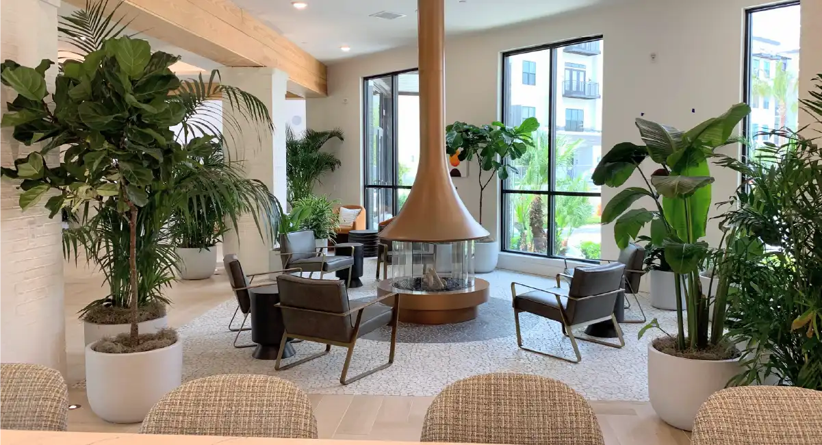 Modern lobby featuring large indoor plants, comfortable seating, and a central fireplace.