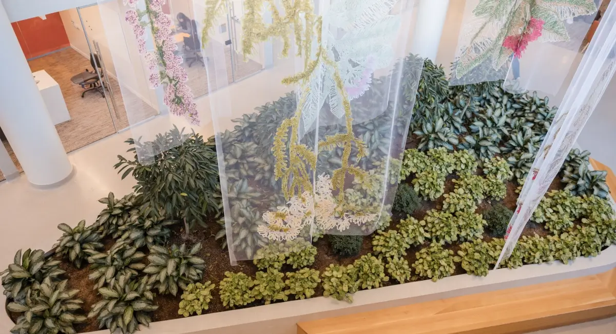 High-angle view of a decorative indoor planter featuring various green foliage and hanging floral art.