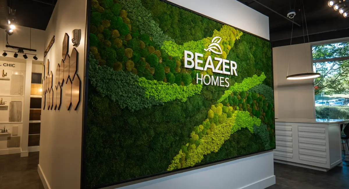 A large, multi-textured green moss wall featuring the Beazer Homes logo in a modern office showroom.